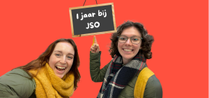 Marit en Juliette wijzen naar een bordje waarop staat 1 jaar bij JSO